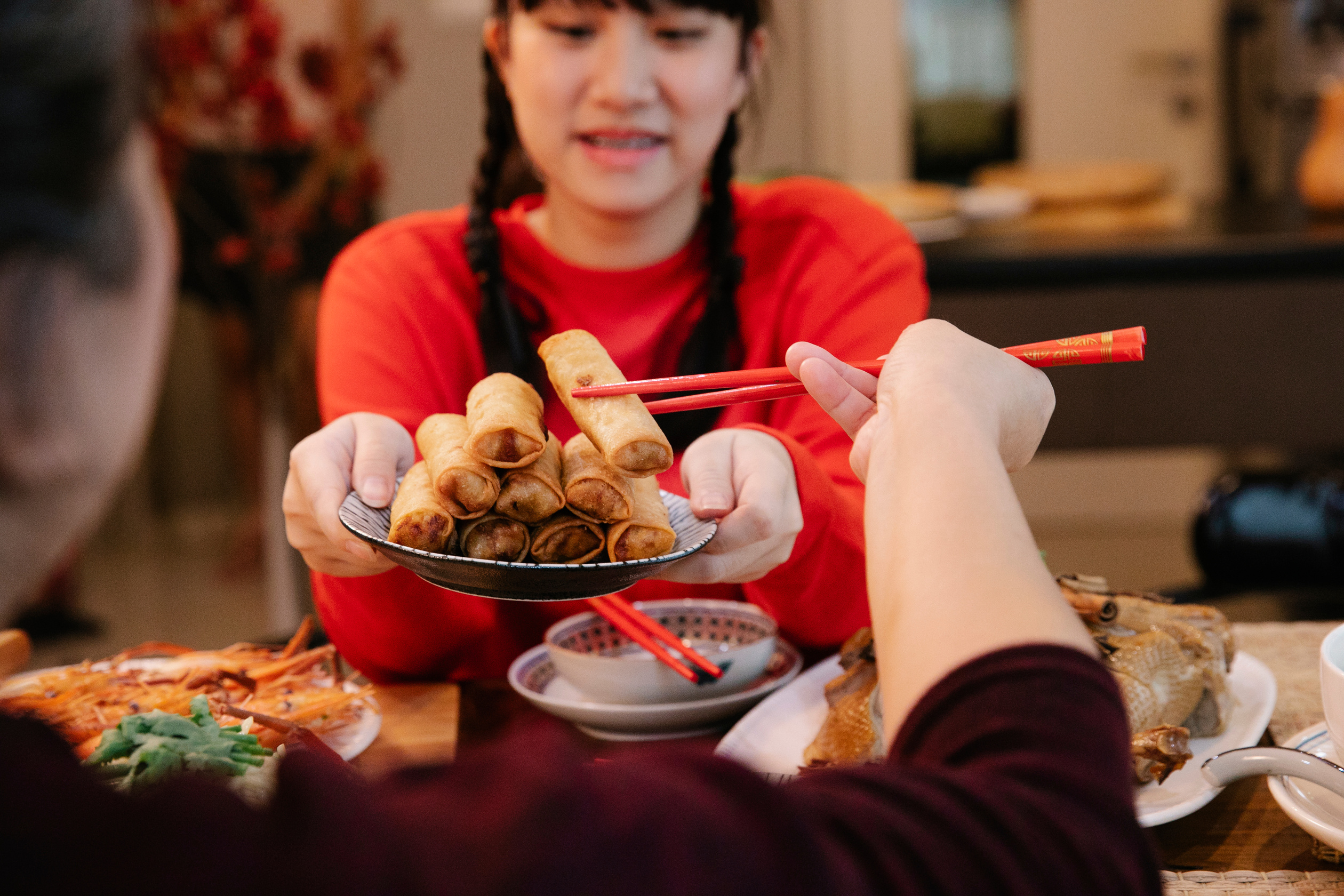Crop ethnic teen serving spring rolls to relative at home